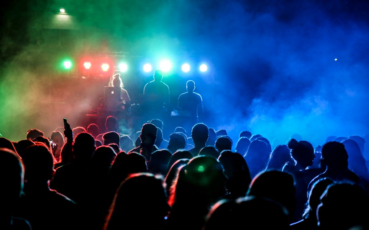 Concert crowd watching a DJ performance beneath colourful lights
