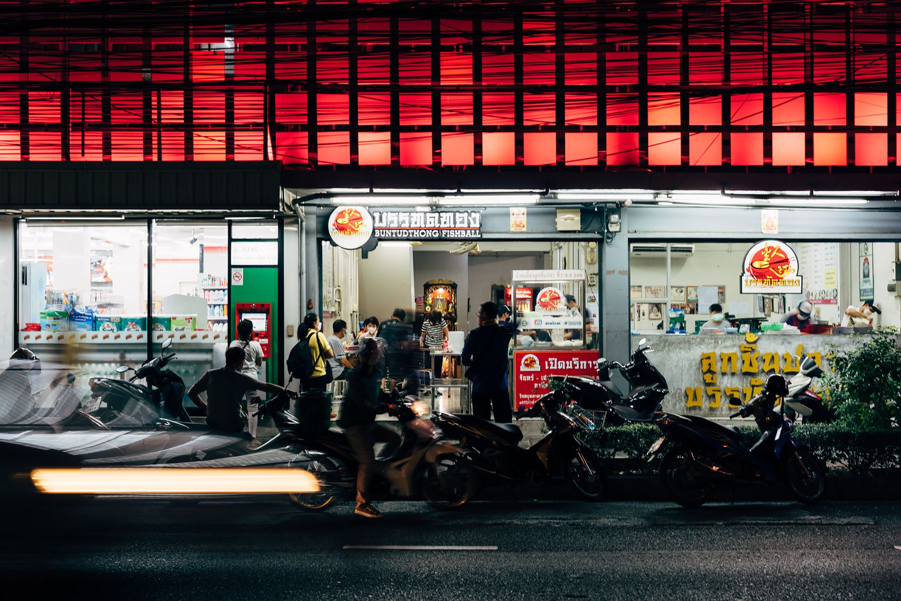 A busy Thai night market with street food and passing motorbikes