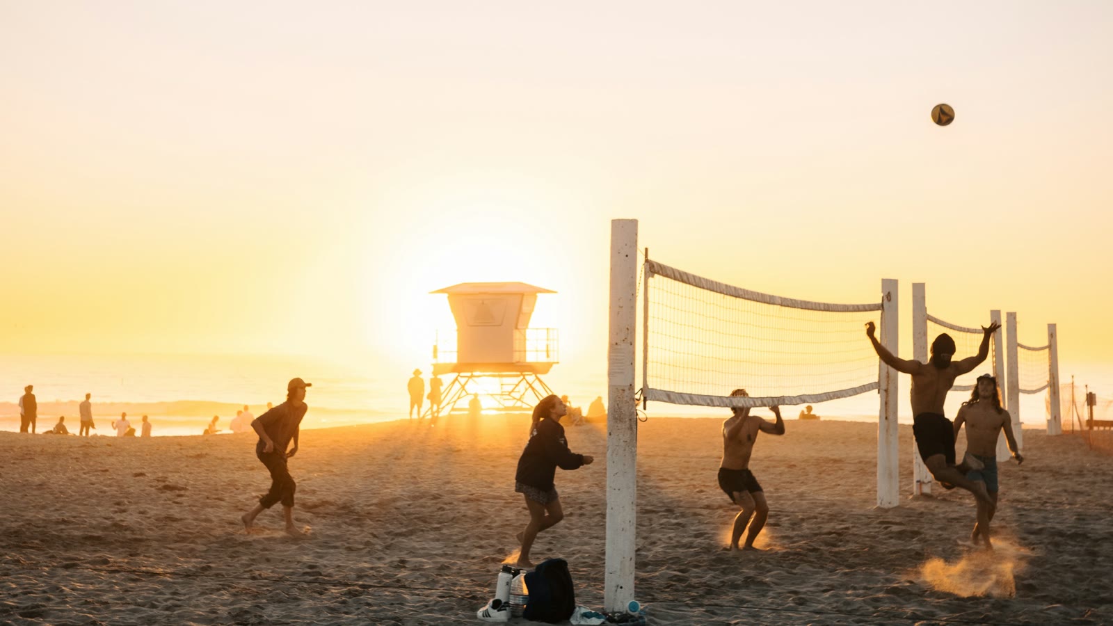 A group playing beach volleyball together at sunset